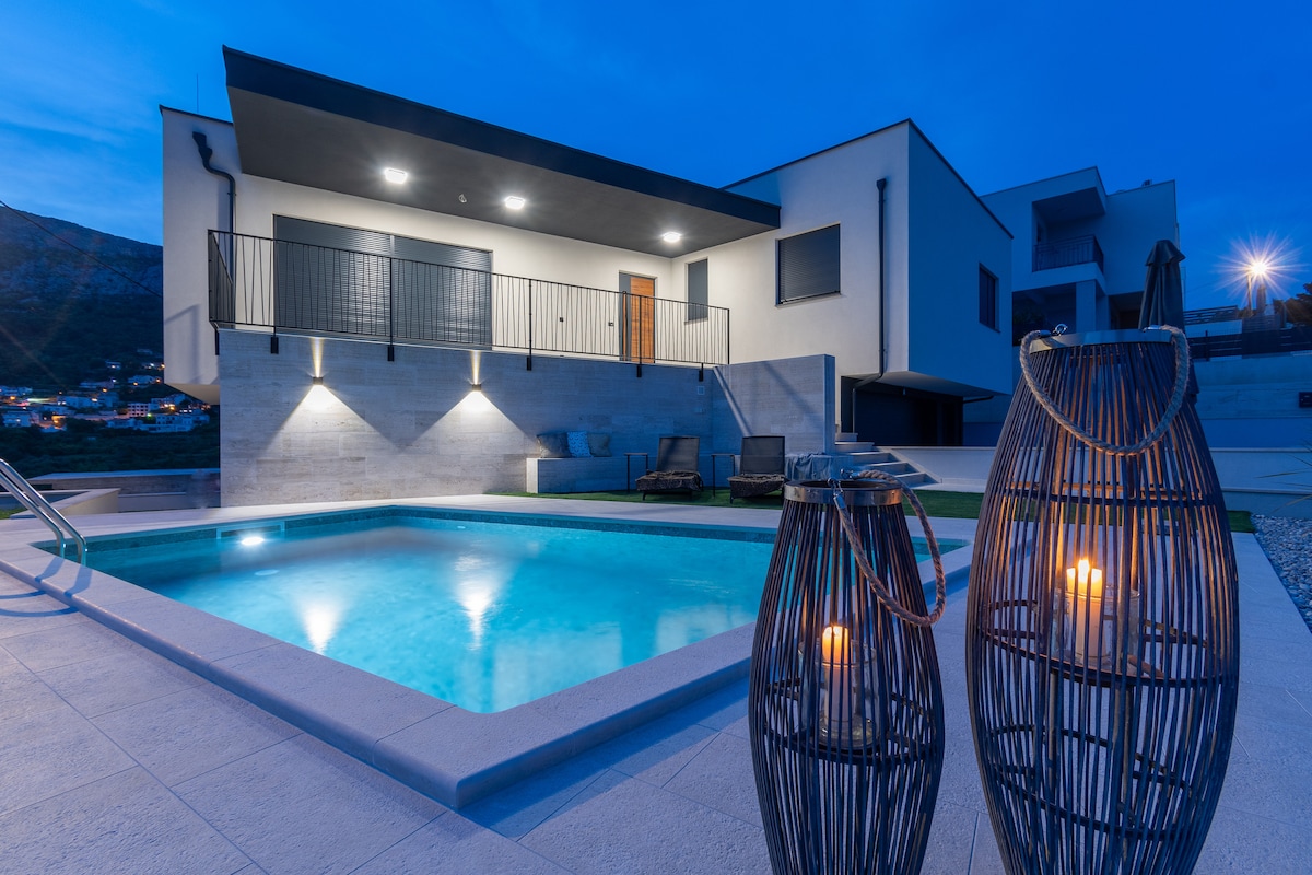 A modern apartment is showcased with a private swimming pool, illuminated against the night sky. Decorative lanterns are placed near the pool's edge, enhancing the tranquil setting. The building features a spacious terrace with seating, providing easy access to the outdoor space.