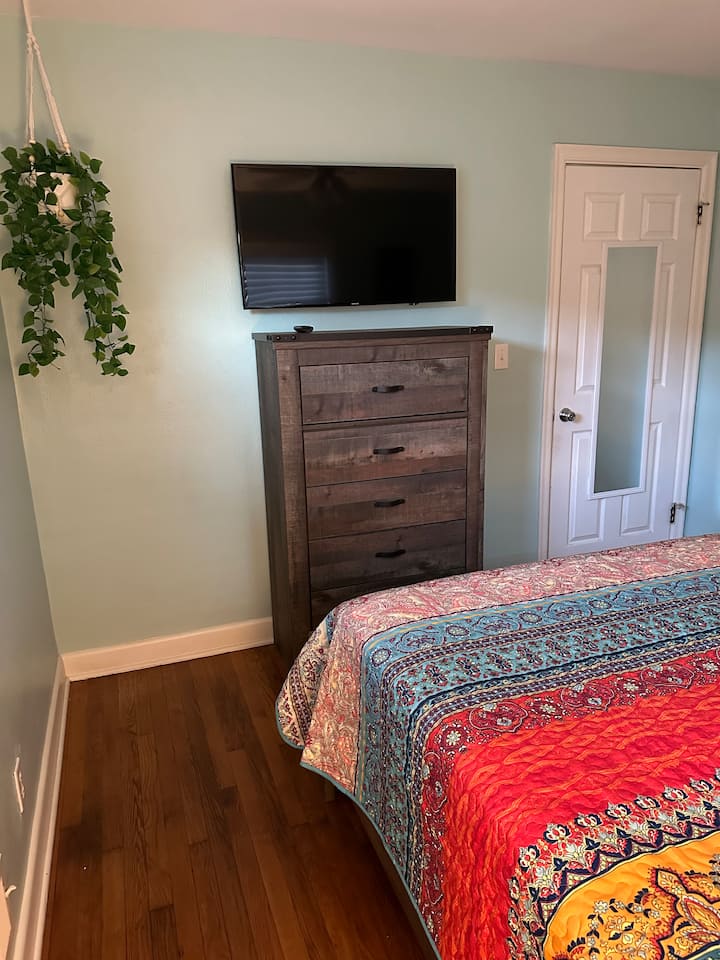 Este quarto tem uma cama queen size, cômoda e armário com cabides.