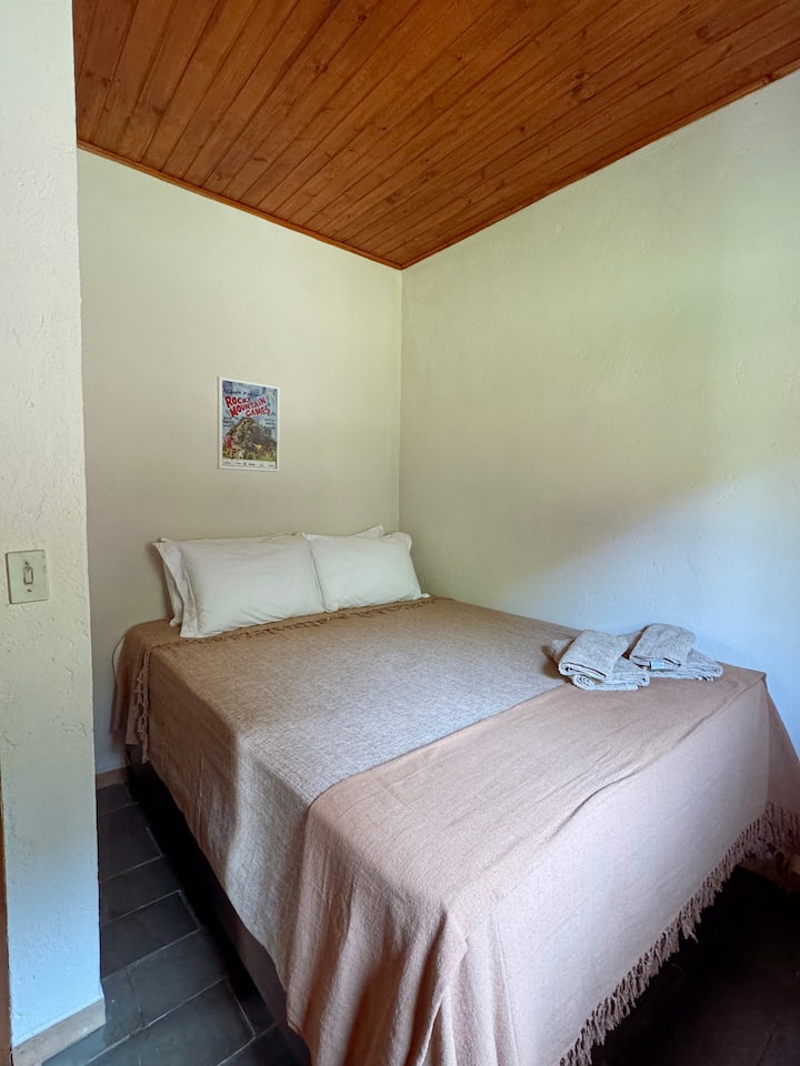 Spálňa s manželskou posteľou Queen, taxíkom a stoličkou v izbe.