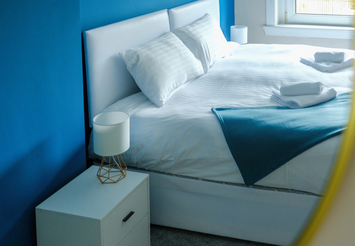 مرحبًا بكم في غرفة النوم 4! تحتوي هذه الغرفة المريحة على سرير مزدوج مع بياضات بيضاء ورمي أزرق مخضر وجدار مزرق. تضيف طاولة جانبية بيضاء مع مصباح ذهبي ومناشف لمسة عصرية. يتدفق الضوء عبر نافذة كبيرة، مما يخلق مساحة مشرقة.