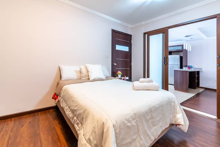 Soba s bračnim krevetom za dvoje ljudi, noćnim ormarićem, plahtama, pokrivačima, jastucima i jastucima za sjedenje, ormarom s vješalicama za odjeću i kaučem.