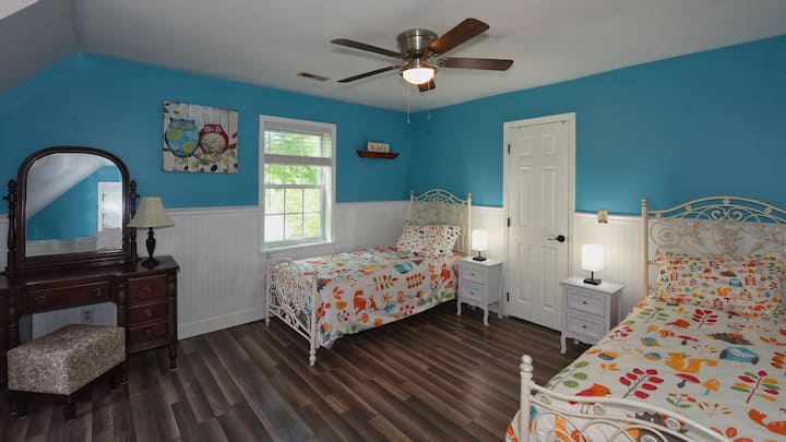 Two twin sized beds in a large west facing room with a desk and Roku tv.