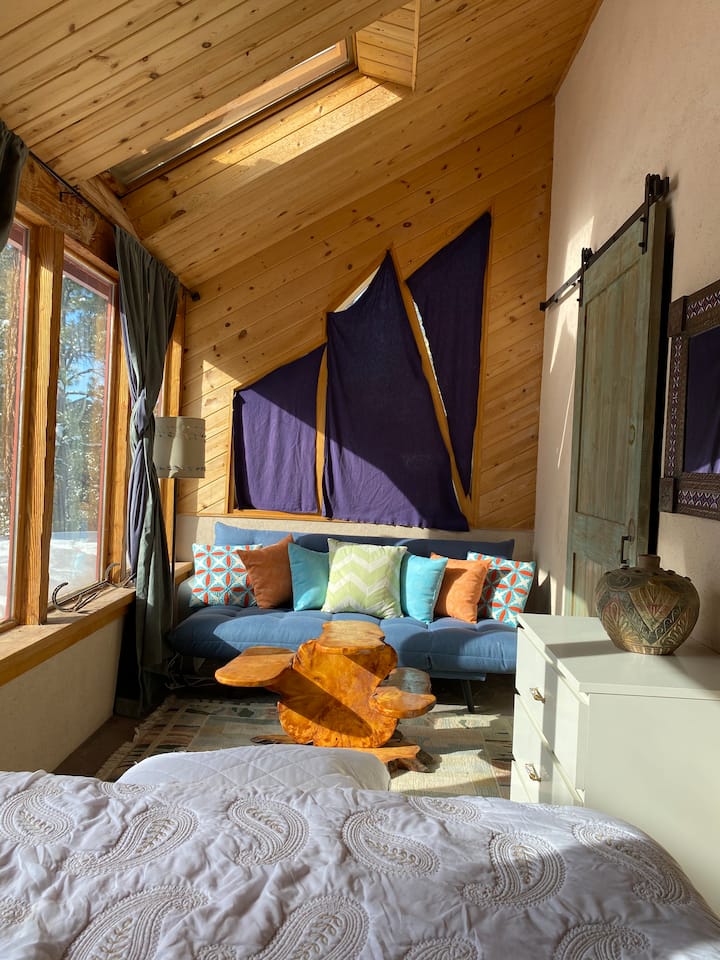 Chumba cha chini cha kulala - sakafu ya mawe iliyozungukwa na madirisha.   Picha ya kitanda/Kochi la bluu la Futon ambayo inaweza kutumika kama sehemu ya ziada ya kulala.