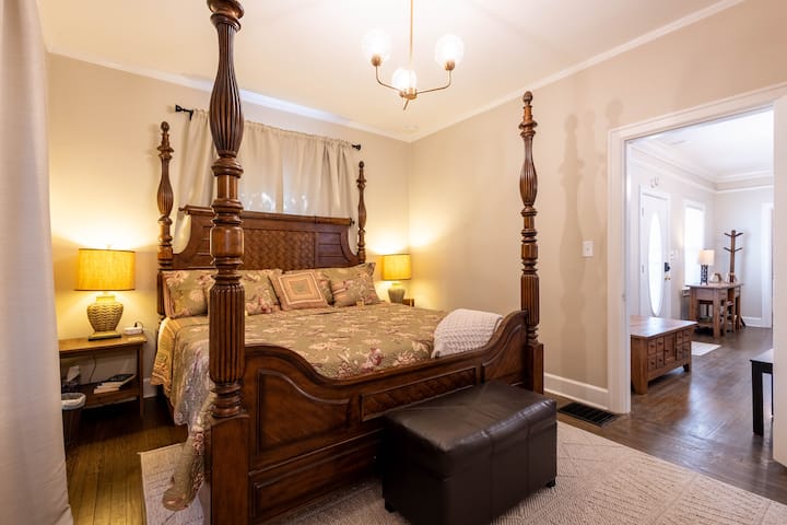 The master bedroom offers wood floors, a cozy king bed, an en-suite bath with tub/shower and vanity, plus a closet with built-in shelves.