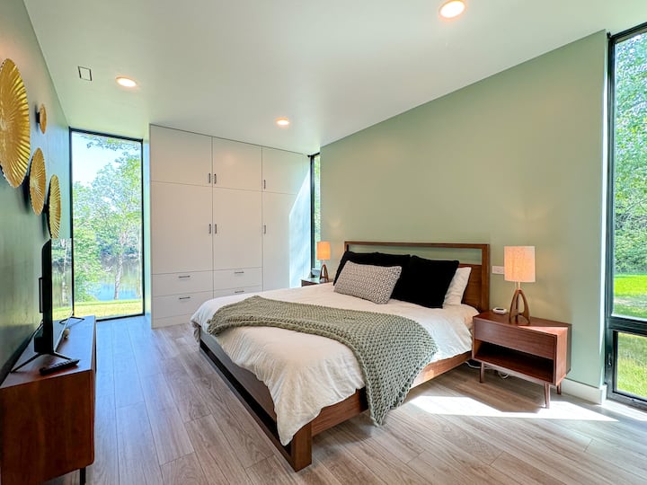 Spacious first-floor master bedroom with stunning floor-to-ceiling windows offering serene views. Includes a comfortable king-sized bed, TV for relaxing evenings, and ample closet space. Attached is a private master bathroom for added convenience.