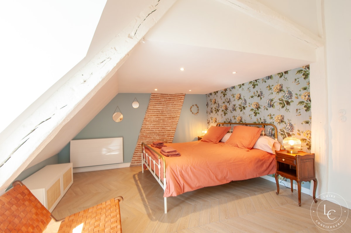 Chambre spacieuse sous les combles avec lit queen size. Décorée de briques apparentes et de papier peint floral pour une atmosphère cosy. Une douche ouverte élégante complète cette suite parentale, idéale pour un séjour confortable et stylé.