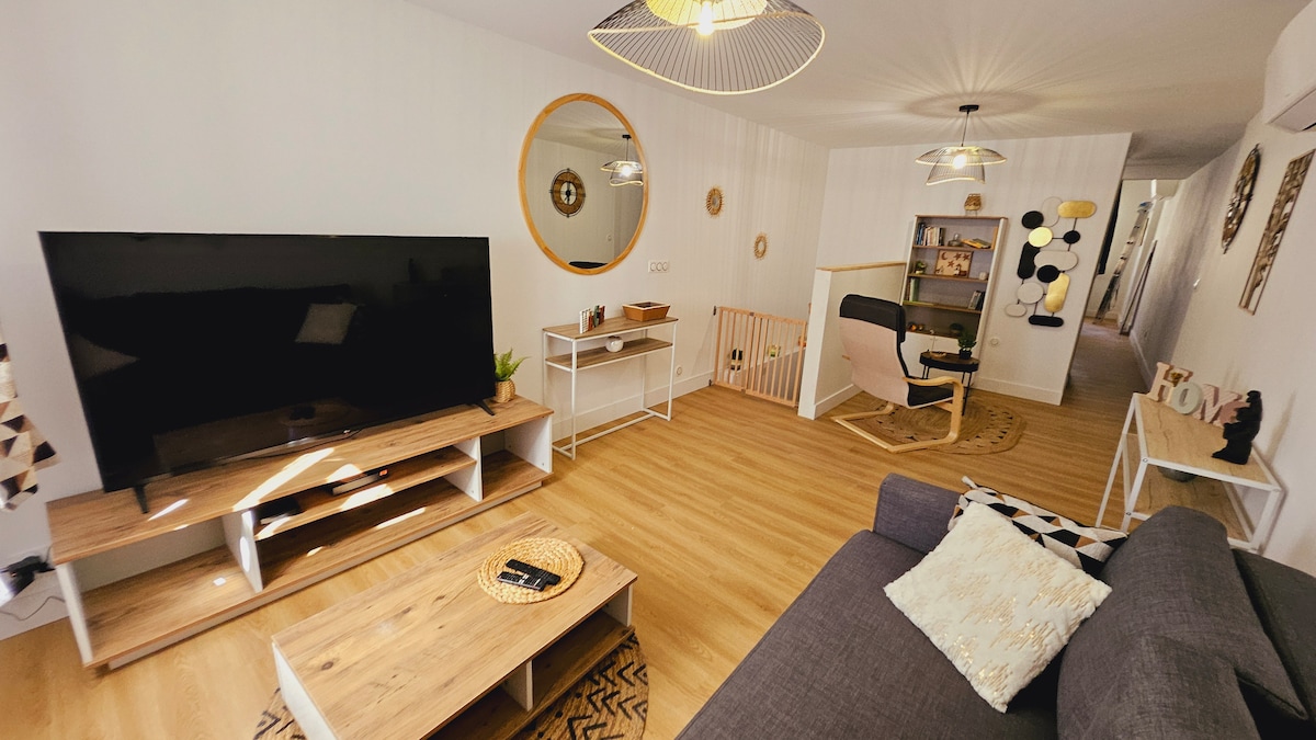 The living area is bright and spacious, showcasing a large television mounted on a wooden console. A comfortable sofa is complemented by a round mirror and decorative accents. A children's play area is visible, featuring soft furnishings and playful decor.