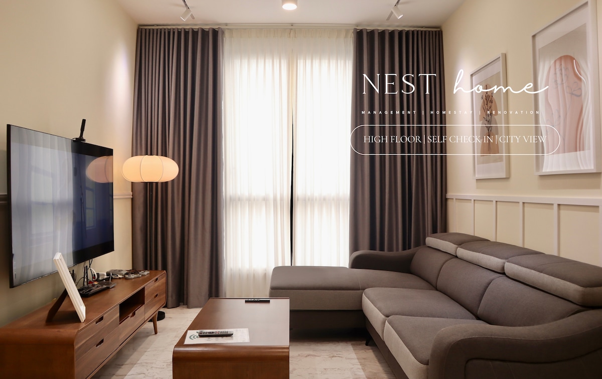 A comfortable living area is presented with a sectional sofa facing a large wall-mounted television. Soft curtains diffuse natural light, while framed artwork adorns the walls. A wooden coffee table is positioned in front, contributing to a relaxed ambiance.