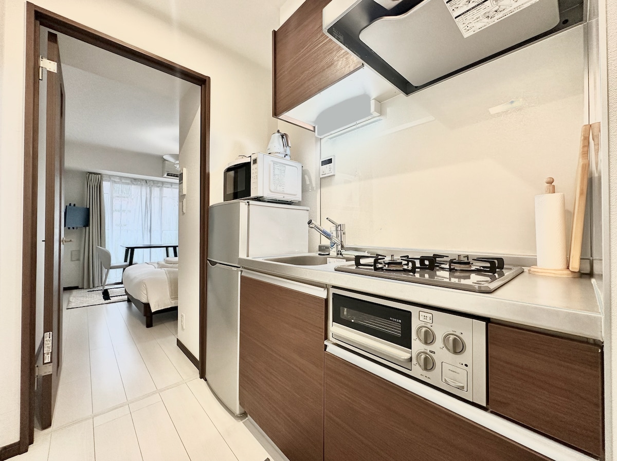 The kitchen area is equipped with modern appliances, including a refrigerator and a gas stove. Counter space accommodates additional kitchenware, and a microwave is prominently placed for convenience. A doorway leads to the adjacent living space, where natural light is enhanced by large windows.