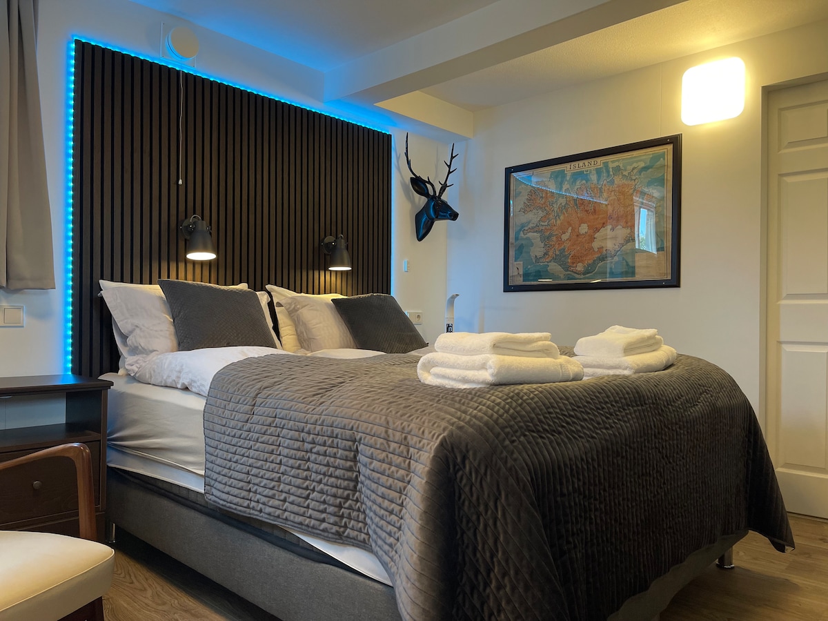 The sleeping area includes a spacious bed framed by wooden paneling and features soft bedding. Wall-mounted lights provide illumination above the bed. A world map is displayed prominently, adding a touch of exploration. Decorative towels are neatly arranged on the bed.