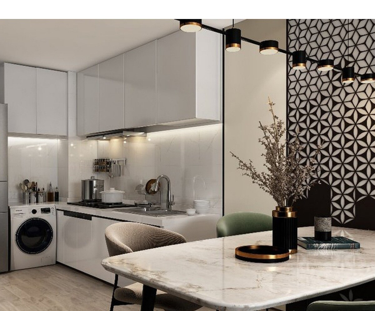 A modern kitchen is equipped with sleek cabinetry and stainless steel appliances, including a washer and dryer. A dining table with a marble surface and stylish chairs is positioned nearby, complemented by a decorative arrangement of dried flowers in a chic vase.