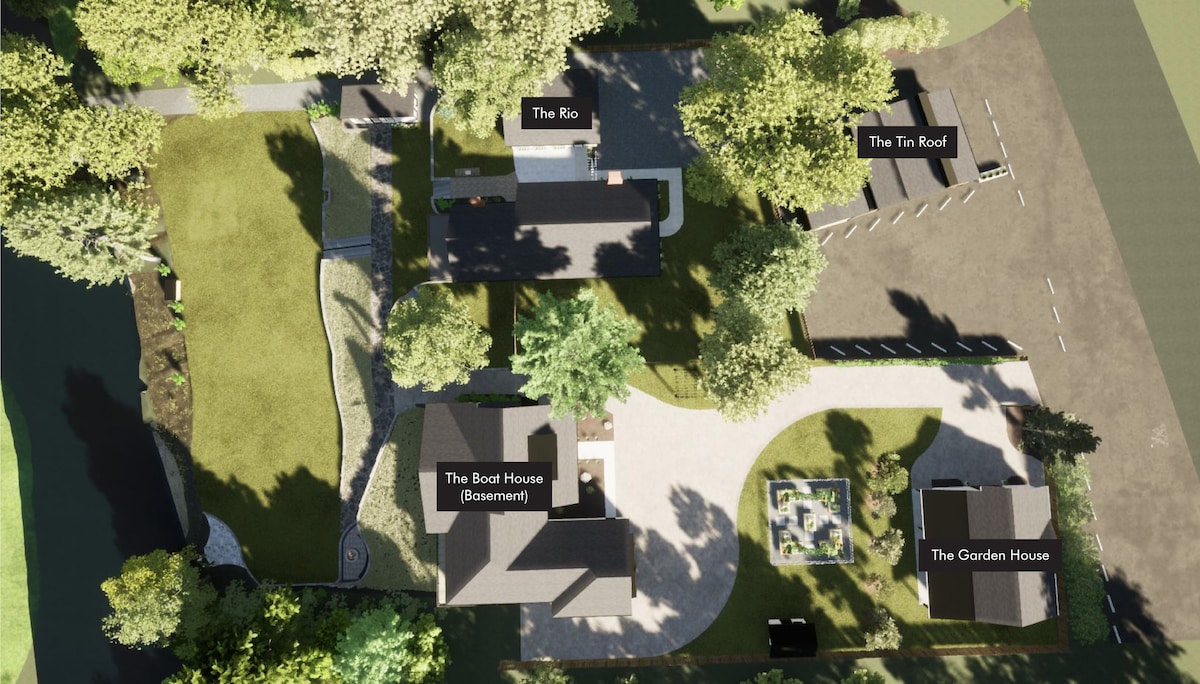 An aerial view of the property showcases multiple buildings, including The Rio, The Tin Roof, The Boot House, and The Garden House. Lush greenery surrounds the structures, and well-maintained pathways connect various outdoor spaces. Ample parking is visible, indicating ease of access to the homes.