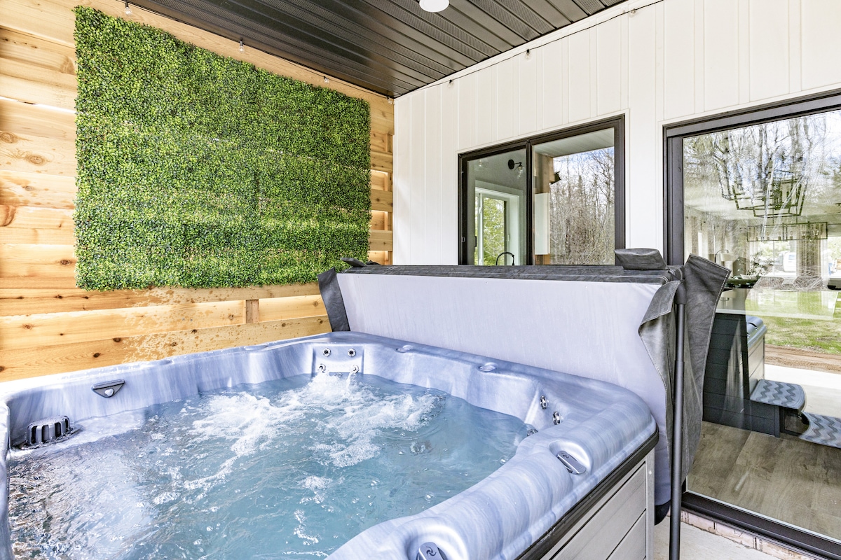 A hot tub is situated against a wooden wall with vertical greenery, providing a relaxing atmosphere. Large sliding glass doors offer a view of the outdoor space, enhancing the connection between indoor and outdoor living.