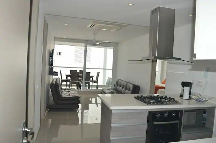 Cocina abierta con Isla,  sillas tipo barra y sala con aire acondicionado y ventilador, salida a la terraza donde esta ubicado el comedor