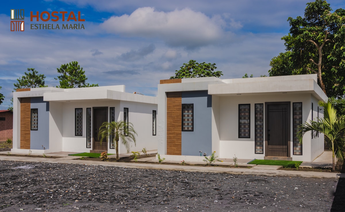 Two modern, single-story suites are depicted, featuring clean lines and a minimalist design. Each suite has large windows with a combination of dark frames and frosted glass. Lush greenery and small shrubs are visible outside, enhancing the natural setting.
