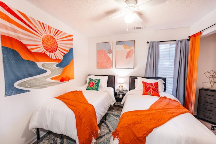 Vitajte v našej pulzujúcej spálni s oddelenými posteľami, ktorá je ideálna na útulné útočisko. Dvojité matrace lemujú centrálny nočný stolík s lampou. Živá bohémska výzdoba a plyšový koberec dodávajú farbu a pohodlie a vytvárajú príjemný priestor na pokojný nočný spánok.