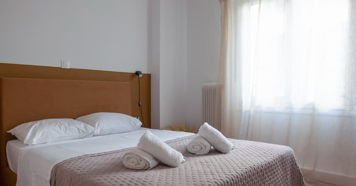 Útulná spálňa s mäkkou, neutrálnou farebnou schémou. Posteľ je úhľadne usporiadaná s čistou posteľnou bielizňou a uterákmi. Veľké okno prepúšťa dostatok prirodzeného svetla a vytvára jasnú a príjemnú atmosféru ideálnu na oddych.

