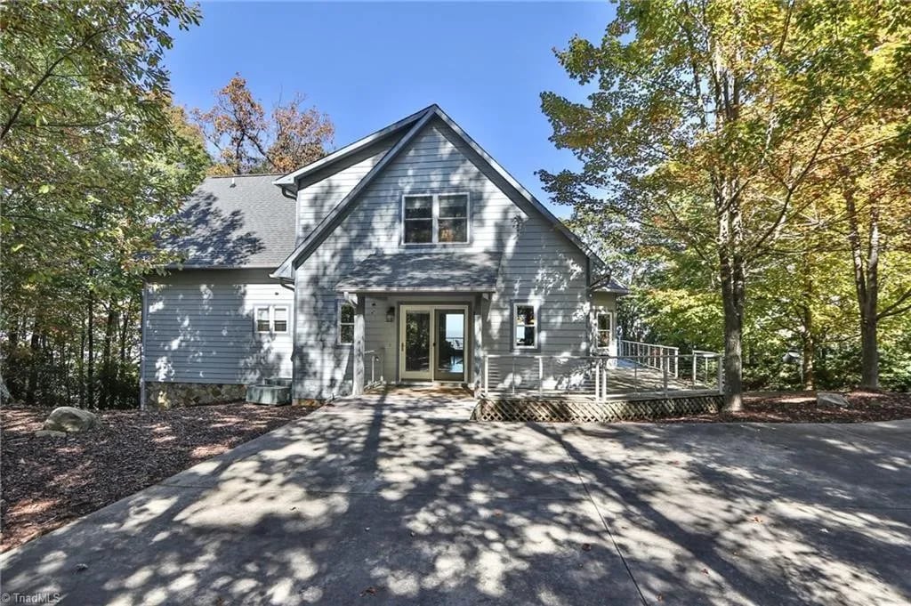 The exterior of a modern two-story home is set against a backdrop of vibrant autumn foliage. A spacious driveway leads to a welcoming entrance. Large windows and a front deck provide access to nature, inviting guests to enjoy the peaceful surroundings.