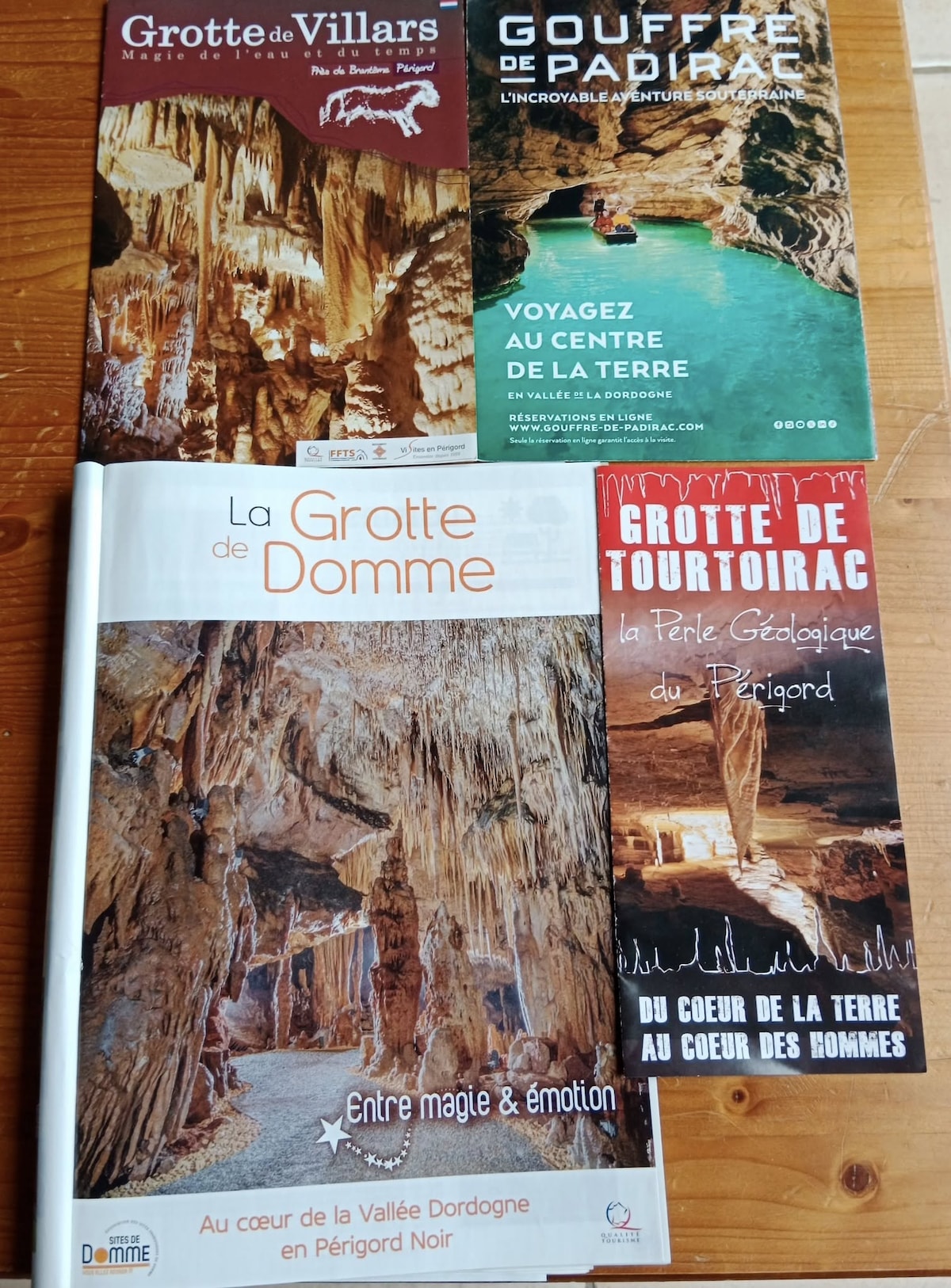 Several travel brochures displaying local attractions are arranged on a wooden surface. Each brochure showcases a different cave in the region, featuring captivating photographs and informative text about the natural wonders of the Dordogne and surrounding areas.
