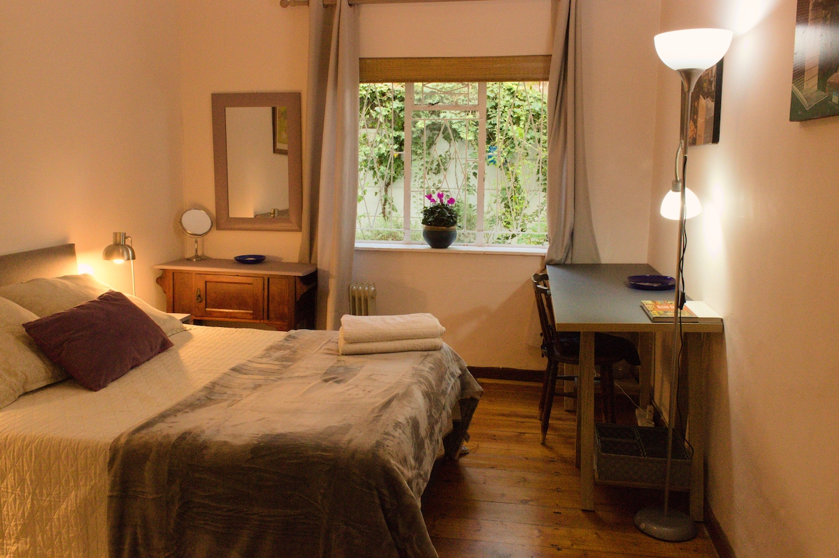 Chumba kina hewa safi kwa sababu ya dari za juu na dirisha ambalo linaangalia nje kwenye njia ya kijani kibichi 