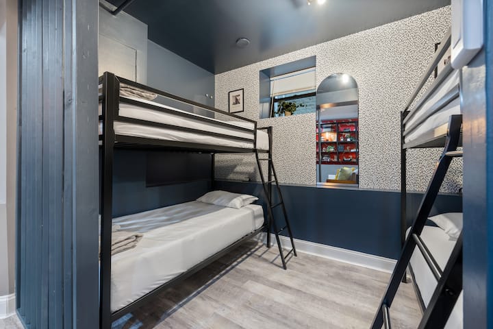 Spavaća soba s krevetima na kat, zidom s tapetama i prozorom s pogledom na ulicu.