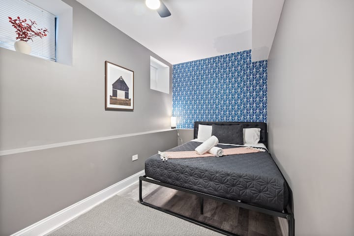 Udobna spavaća soba sa sivim bračnim krevetom, bijelim ručnicima, smeđom foteljom, zelenim vratima, ogledalom i prozorom.