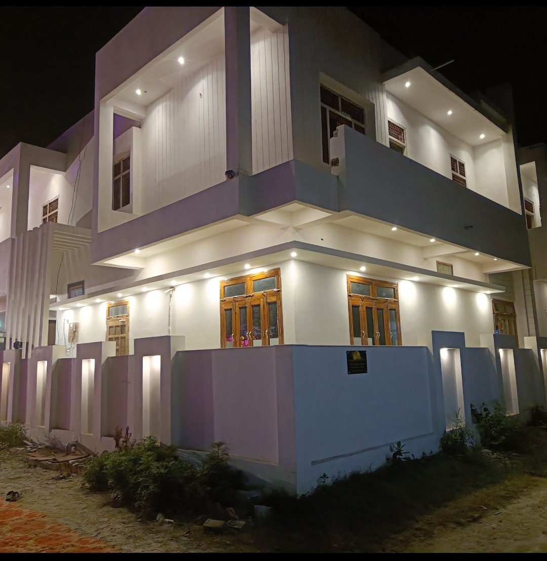 A modern building with a sleek white exterior is showcased at night, highlighted by soft illumination from strategically placed lights. Large windows provide glimpses of the interior, with a well-maintained outdoor area featuring low greenery and a neat pathway.