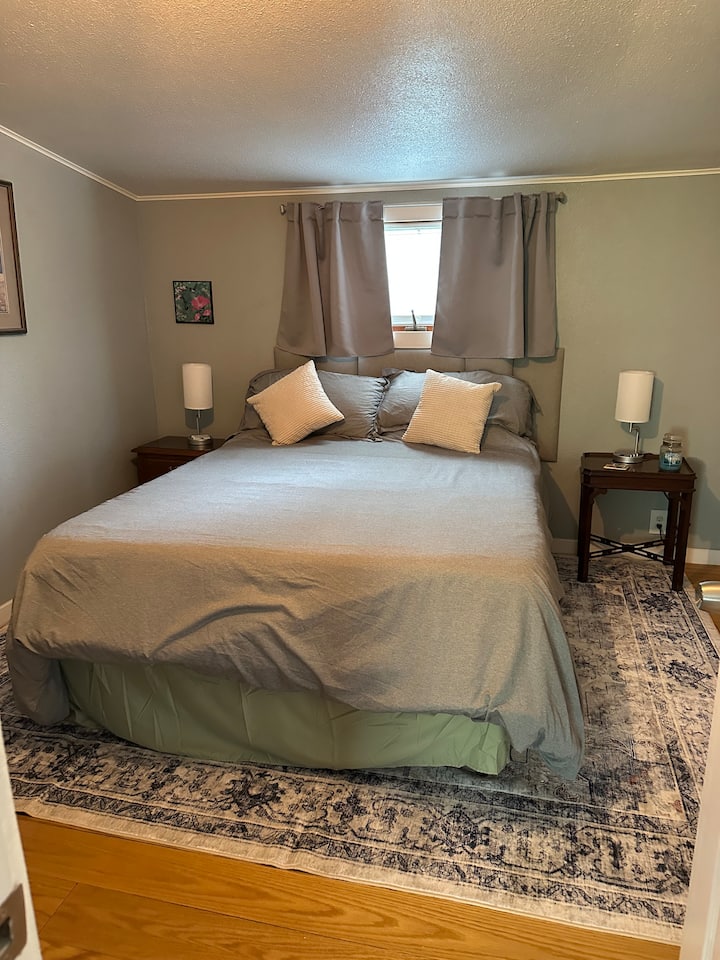 Queen bed, side table lights have charge ports for phones. Smart TV is hung on the opposite wall.