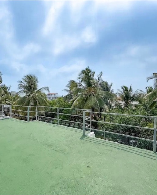 A spacious rooftop deck is presented, featuring a green surface that contrasts with the lush palm trees surrounding the area. A clear sky is visible overhead, enhancing the openness of the space.