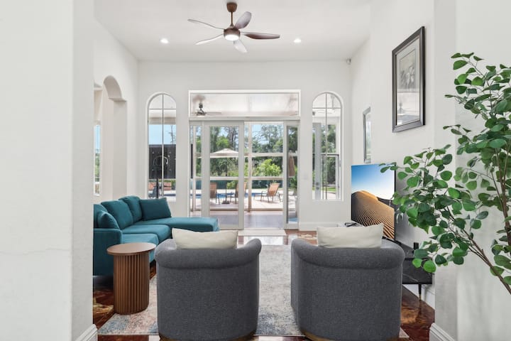 Unwind in this inviting family room featuring plush seating, a large-screen TV, and panoramic views of the pool and garden. A perfect space to relax, connect, and enjoy the indoor-outdoor vibe.