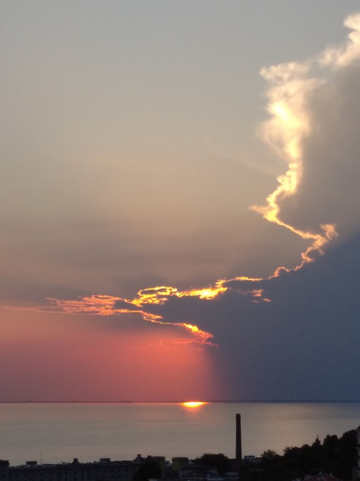 A serene sunset over the sea is captured, with hues of orange and pink fading into the blue sky. The sun's reflection glimmers on the water's surface, while wispy clouds frame the scene, creating a calming atmosphere.