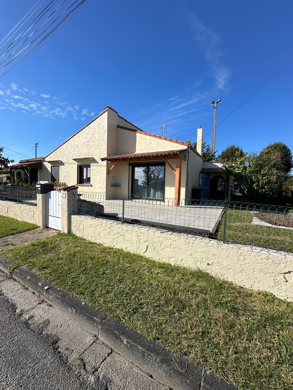 A renovated single-story house features a charming exterior with a textured yellow facade. Large windows provide natural light, while a tiled roof contributes to the overall character. A well-maintained lawn and low fence outline the property, enhancing its inviting appearance.
