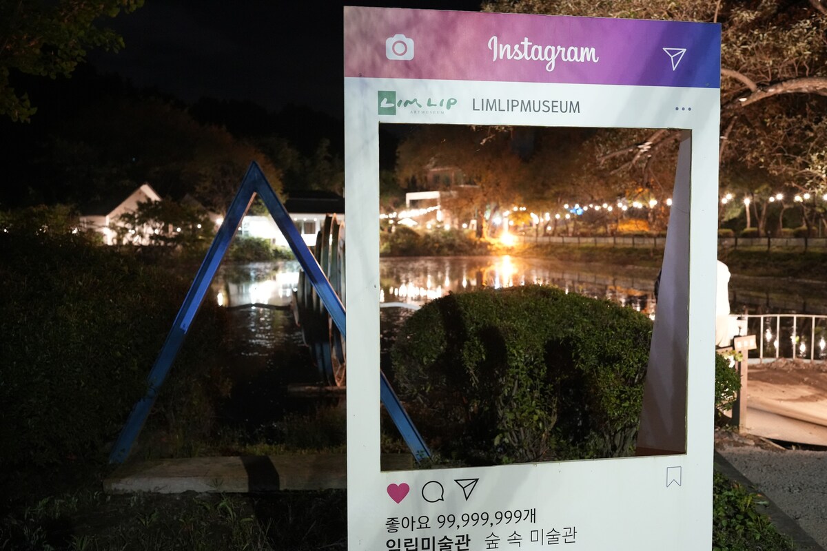 An Instagram photo frame sets the scene in front of a serene water view at night, reflecting soft lights from surrounding trees and structures. The ambient glow creates a tranquil atmosphere, inviting guests to capture their experiences in this peaceful setting.