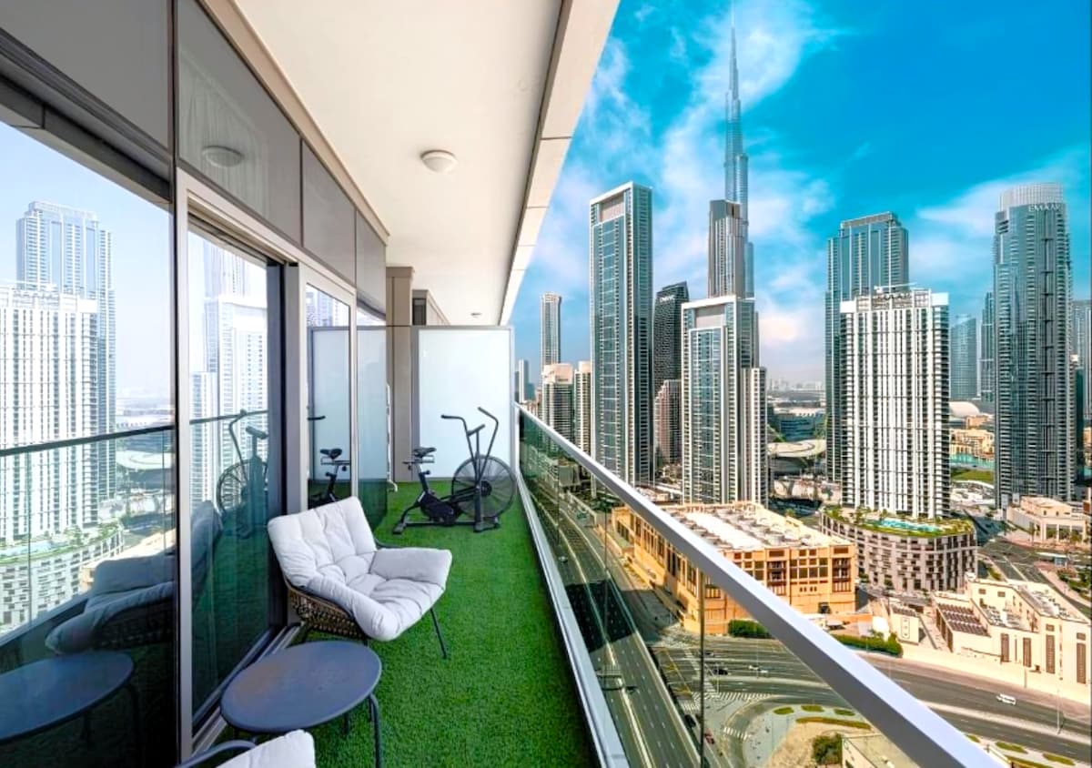 A spacious balcony features a turf surface, offering a relaxing seating area with two cushioned chairs and a small table. A panoramic view showcases the Burj Khalifa along with the vibrant Downtown skyline, allowing guests to enjoy the surrounding urban landscape.
