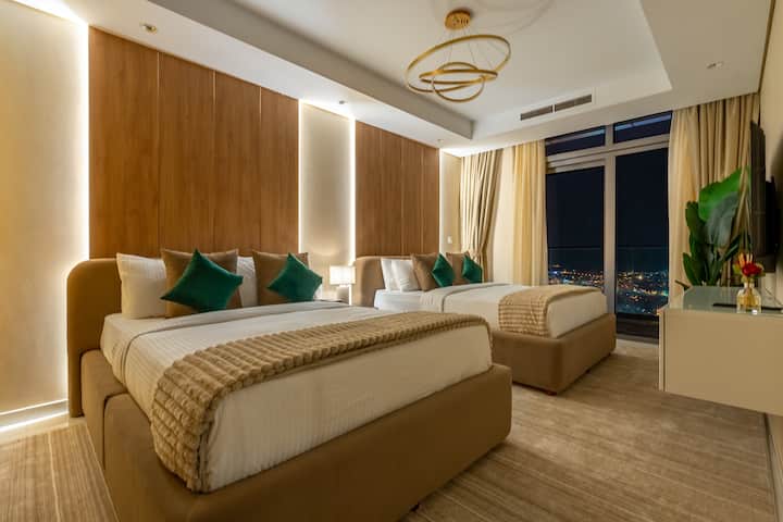 חדר שינה נעים עם שתי מיטות נוחות, תאורה חמה ואווירה מרגיעה בלילה. מקום מפלט מושלם לשהייה נינוחה, המשלבת נוחות וסגנון מודרניים בלב מרכז העיר דובאי.