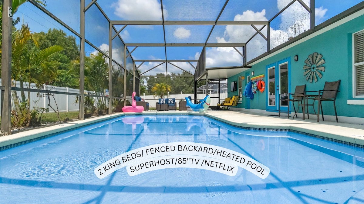 A spacious pool area is enclosed with a protective screen, featuring a crystal-clear swimming pool. Surrounding the pool are comfortable lounge chairs and colorful inflatables, providing a relaxing environment. The backyard is fenced for privacy, enhancing the serene atmosphere.
