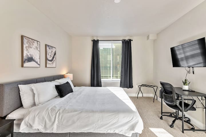 Habitación luminosa con escritorio, televisor de pared y luz natural por la ventana para una estadía cómoda