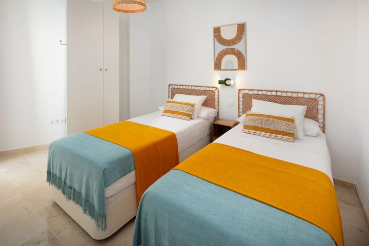 Segundo quarto com duas camas de solteiro com roupa de cama de hotel, guarda-roupa e pequena varanda para o suporte de secagem.