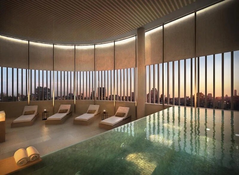 A serene spa area features a large indoor pool with reflective water, surrounded by comfortable lounging chairs. Tall windows provide a view of the city skyline at sunset, allowing soft light to fill the space.
