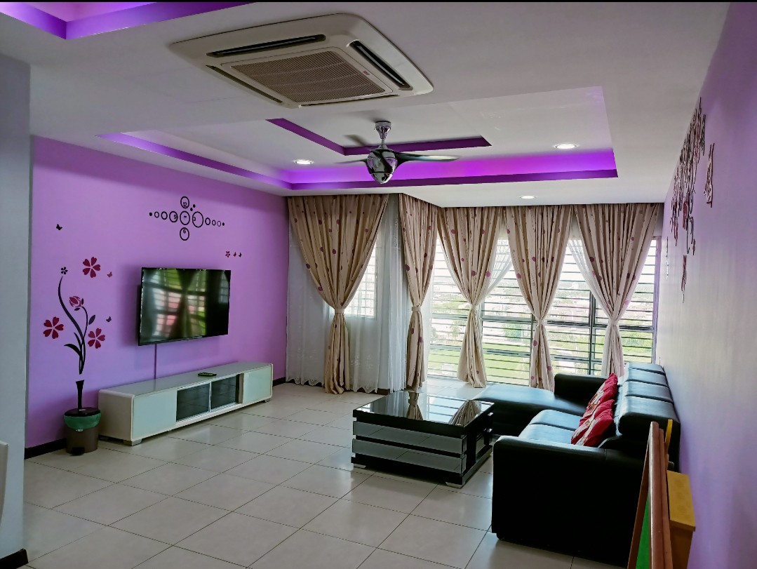 A spacious living area is filled with natural light from wide windows, featuring a black sectional sofa adorned with colorful cushions. A wall-mounted television is positioned across from the seating. Purple accent lighting adds a touch of modernity to the room's design.