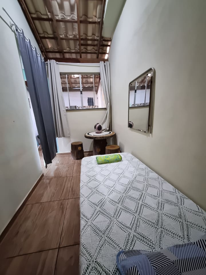 Საძინებელი ერთადგილიანი საწოლით და პატარა მაგიდით, სარკით, აქვს ფანჯარა და უშუქო ფარდა.