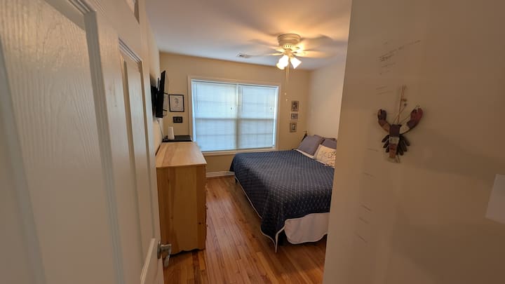 Მთავარი საძინებელი პირველ სართულზე ტელევიზორით, ვენტილატორით, კომოდითა და კარადა საკიდებით.