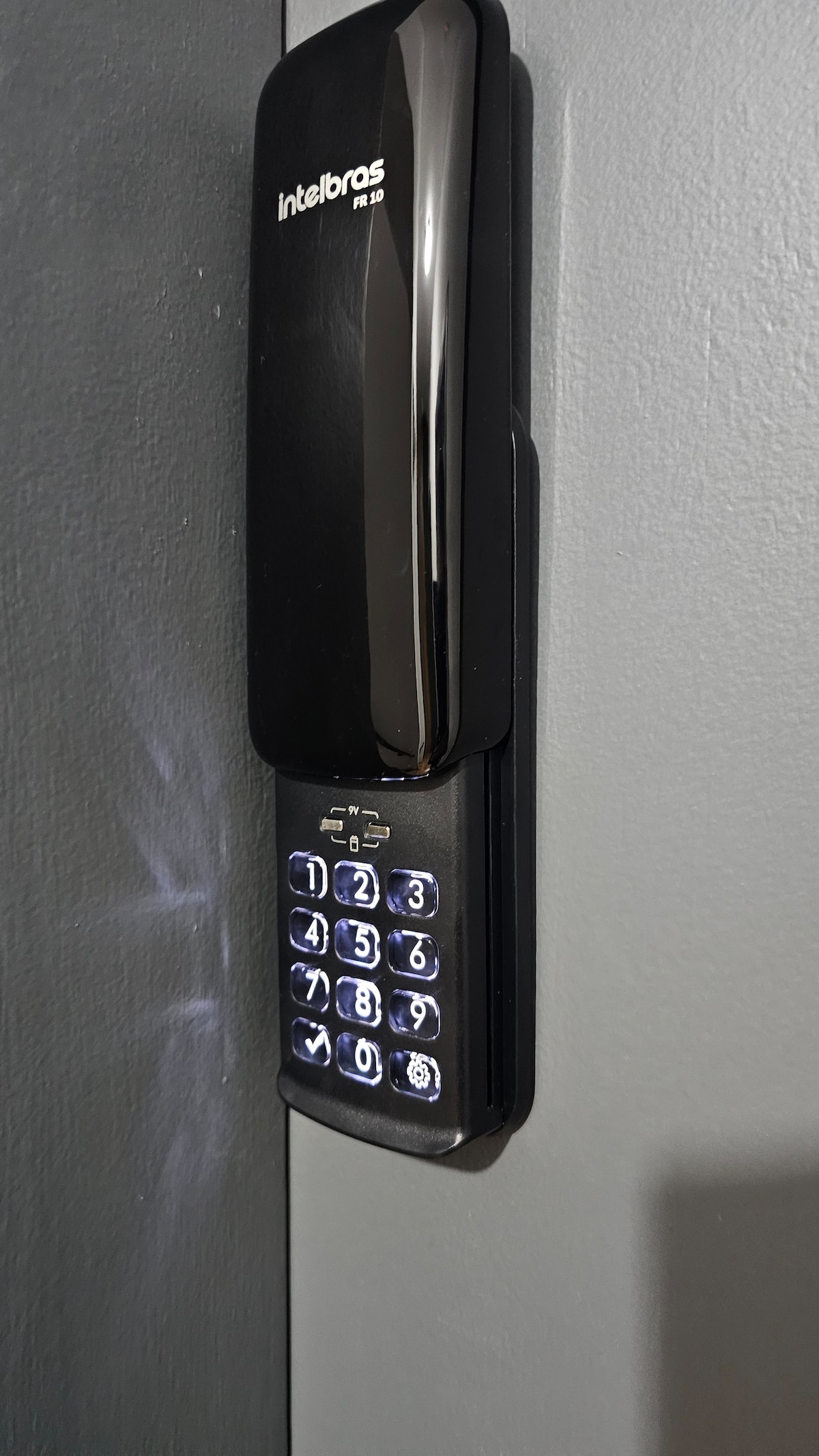 A modern electronic keypad is mounted on a wall, featuring a sleek black design with illuminated numbers. The keypad is positioned beside a gray door, indicating secure access to the studio.
