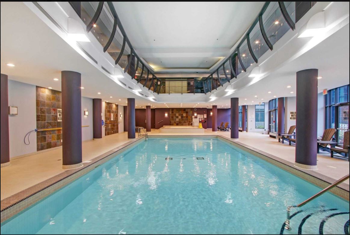 An indoor swimming pool is featured, surrounded by tall windows that allow natural light to illuminate the space. Comfortable lounge chairs are arranged along the pool's edge, and decorative walls add a touch of elegance to the area.