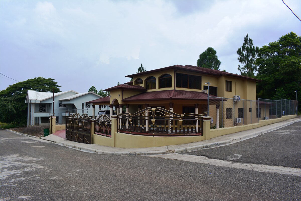 A two-story home is featured on the corner of a quiet street, showcasing a mix of architectural styles. The exterior is painted in warm tones with multiple windows and an inviting entrance adorned with a decorative fence.