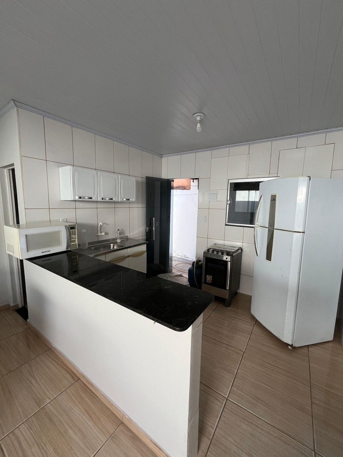 The kitchen features modern appliances including a refrigerator, microwave, and gas stove. Countertops are finished in dark granite, complemented by white cabinetry. Natural light fills the space through a window, creating a well-lit cooking area.