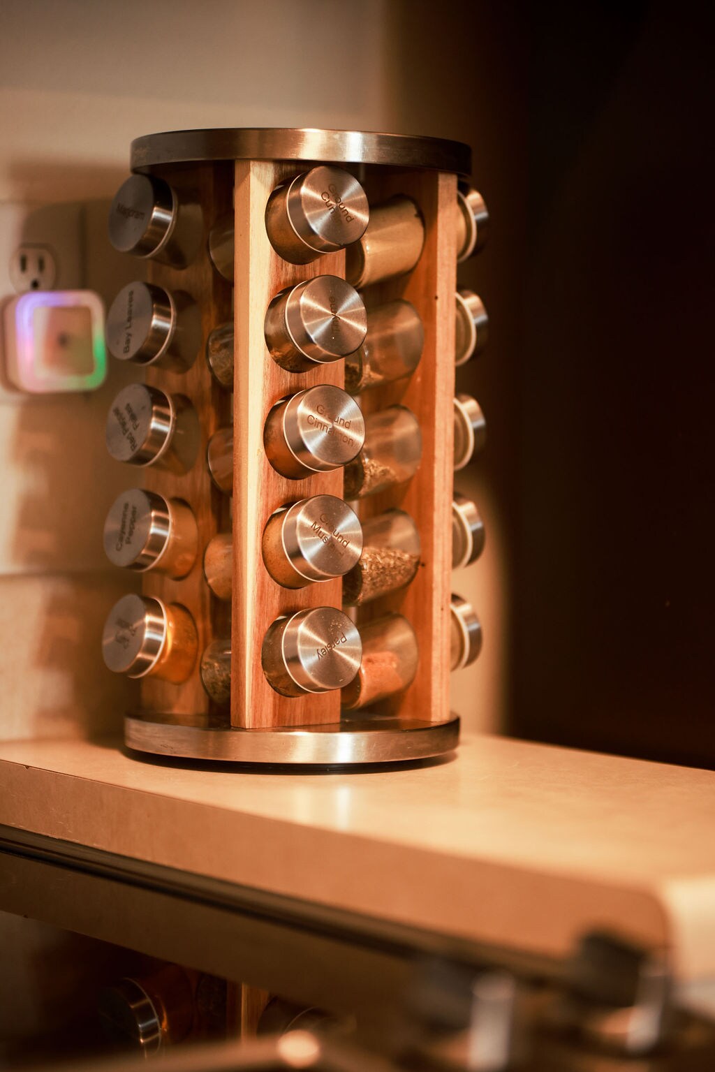A wooden spice rack is positioned on a countertop, featuring several glass jars with metallic labels. The rack displays an assortment of spices, adding functionality to the kitchen space.