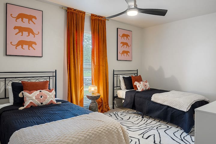 This bedroom is designed for comfort with two twin beds, vibrant artwork, and ample natural light. The ceiling fan ensures a pleasant stay.