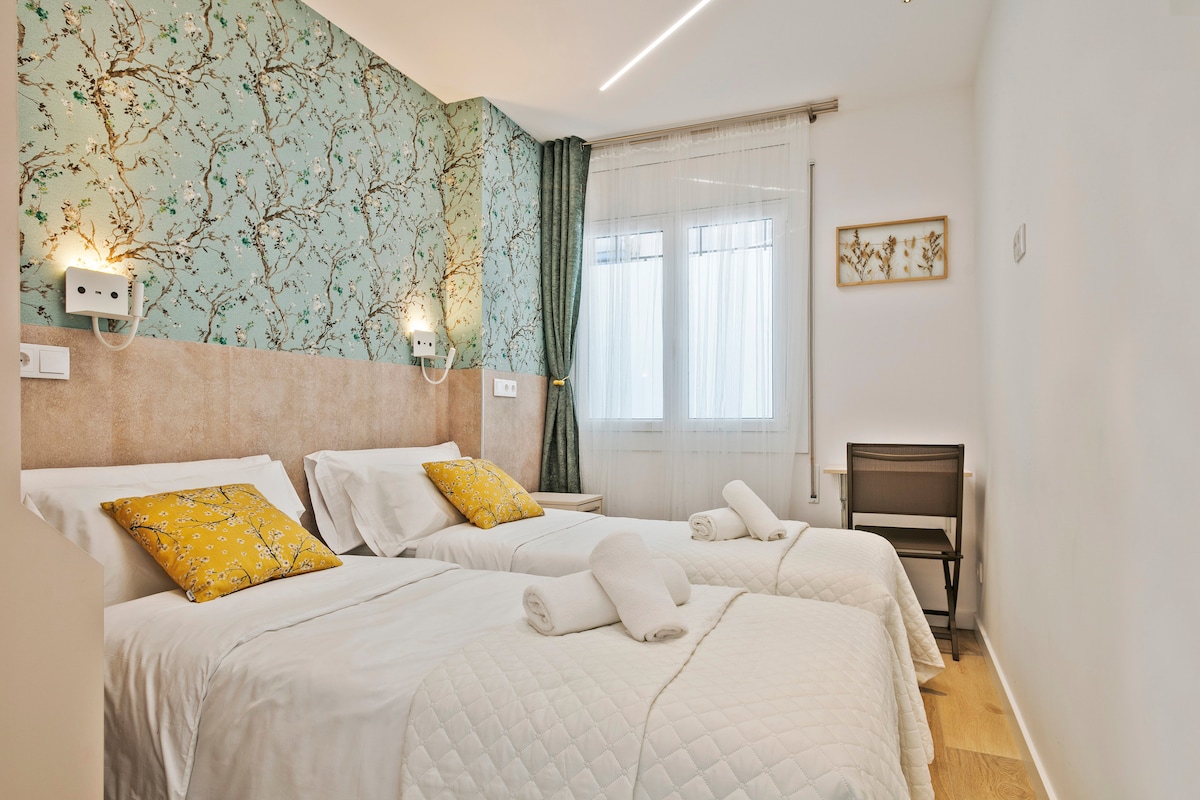 Este dormitorio acogedor resalta por su papel tapiz floral y cojines coloridos. Las camas gemelas son cómodas y la cortina verde añade frescura. Un espacio perfecto para un descanso tranquilo en un ambiente sereno.