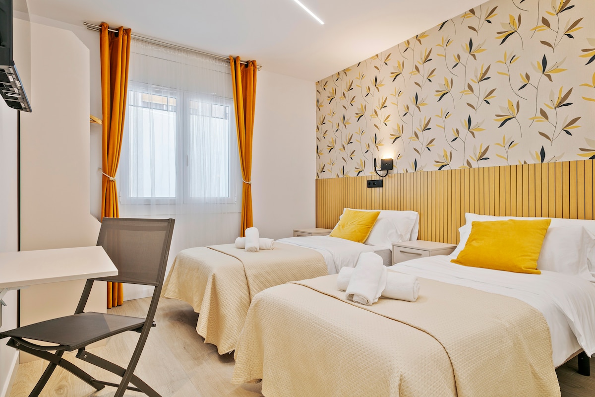 Este dormitorio doble destaca por su diseño alegre, con papel tapiz de motivos naturales y cortinas mostaza que añaden vitalidad. Las camas gemelas, vestidas con suaves textiles, crean un ambiente cómodo y relajante para un descanso óptimo.